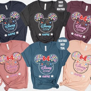 a collection of Disney-themed t-shirts in various colors, including navy, dark gray, maroon, peach, and teal. The t-shirts feature the iconic Mickey Mouse ears and the text "Disney 2020" along with the names "HEATHER" and "MAVE" printed on them.