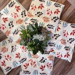 a potted plant with green leaves and a white vase filled with white flowers, placed on a wooden surface. The plant is surrounded by colorful patterned pillows.