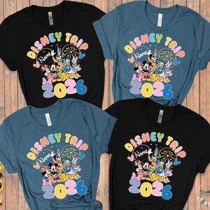 K&ouml;nnte beinhalten: Vier kurz&auml;rmelige T-Shirts in Schwarz und Blau, jedes mit einem farbenfrohen "Disney Trip"-Design mit Mickey Mouse, Minnie Mouse, Donald Duck und anderen Charakteren. Das Jahr "2026" ist deutlich sichtbar.