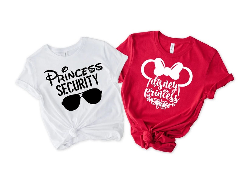 May include: Two white t-shirts with black text and graphics. One shirt says "Princess Security" with sunglasses. The other shirt is red with white text and a white graphic of Mickey Mouse ears with a bow. The text says "Disney Princess".