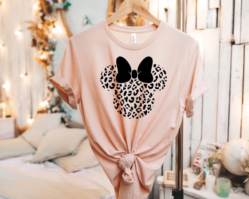May include: A pink t-shirt with a black and white leopard print Minnie Mouse head design. The bow is black.