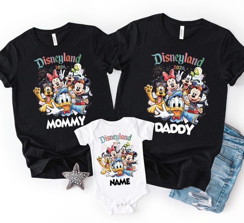 May include: Black t-shirts and a white onesie featuring a colorful graphic of Disney characters. The shirts have "Disneyland 2026" and "Mommy" or "Daddy" printed on them. The onesie has "Disneyland 2026" and "Name" printed on it.
