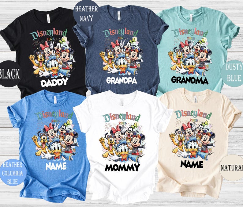 May include: Assorted-color t-shirts with a Disneyland 2026 graphic featuring Mickey Mouse, Minnie Mouse, Donald Duck, and other characters. The shirts are available in black, navy, dusty blue, heather blue, white, and natural colors, with text for family members.