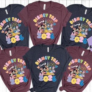 K&ouml;nnte beinhalten: Mehrere Shirts in Heather Navy, Heather Maroon und Dunkelblau. Jedes Shirt zeigt ein farbenfrohes "Disney Trip 2026"-Design mit Mickey Mouse, Minnie Mouse und anderen Disney-Figuren. Rundhalsausschnitt.
