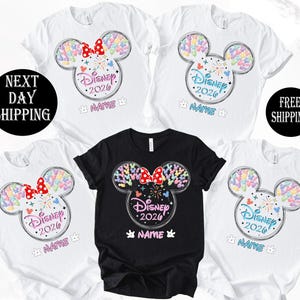 a collection of Disney-themed t-shirts, each featuring a unique design of a Mickey Mouse ear with colorful hearts and the text "Disney 2020". The t-shirts are arranged in a row, with the first one being a black t-shirt and the rest being white t-shirts. The text "Disney 2020" is prominently displayed on each t-shirt, indicating the theme of the shirts.