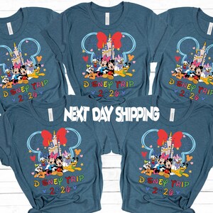 May include: Blue t-shirts with a Disney Trip 2020 design. The graphic features Mickey Mouse, Minnie Mouse, Donald Duck, and other characters in front of a castle. The text "NEXT DAY SHIPPING" is also visible.