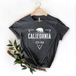 May include: A dark gray t-shirt with a white graphic design featuring a bear, a triangle, and the text "California, The Golden State, Est 1850".