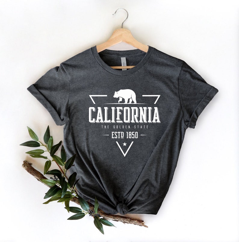 May include: A dark gray t-shirt with a white graphic design featuring a bear, a triangle, and the text "California, The Golden State, Est 1850".