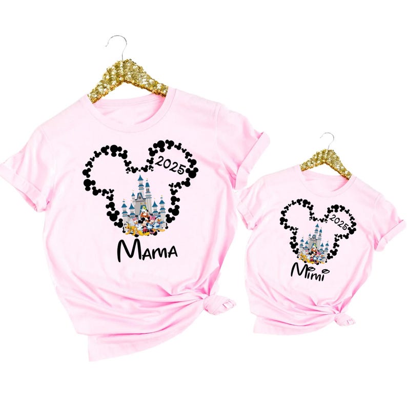 May include: Pink t-shirts with a black Mickey Mouse silhouette design featuring the Cinderella Castle and the text "2025". One shirt says "Mama" and the other says "Mimi".