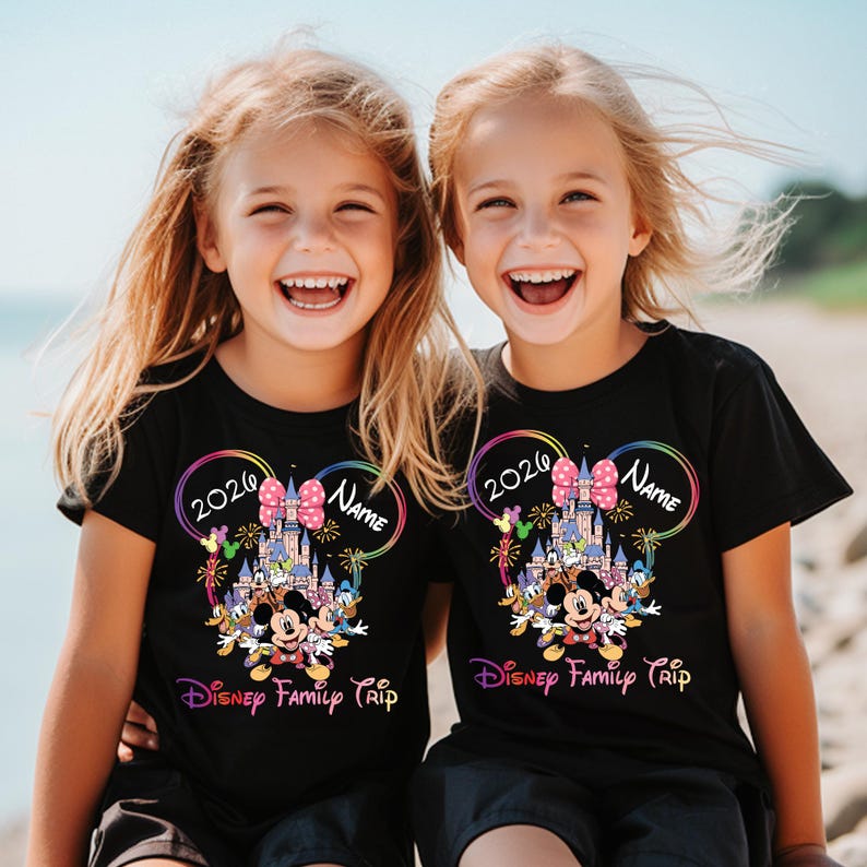 May include: Two children wearing black t-shirts with a colourful Disney design. The design includes a castle, Mickey Mouse, and the text "2020 Name Disney Family Trip". The shirts have a rainbow-coloured Mickey Mouse ear outline.
