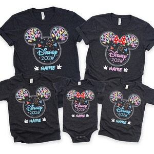 a collection of Disney-themed t-shirts, each featuring a unique design of Mickey Mouse ears and the text "Disney 2020" printed on them. The t-shirts are arranged in a row, showcasing various sizes and styles, likely intended for a family or group of Disney fans.