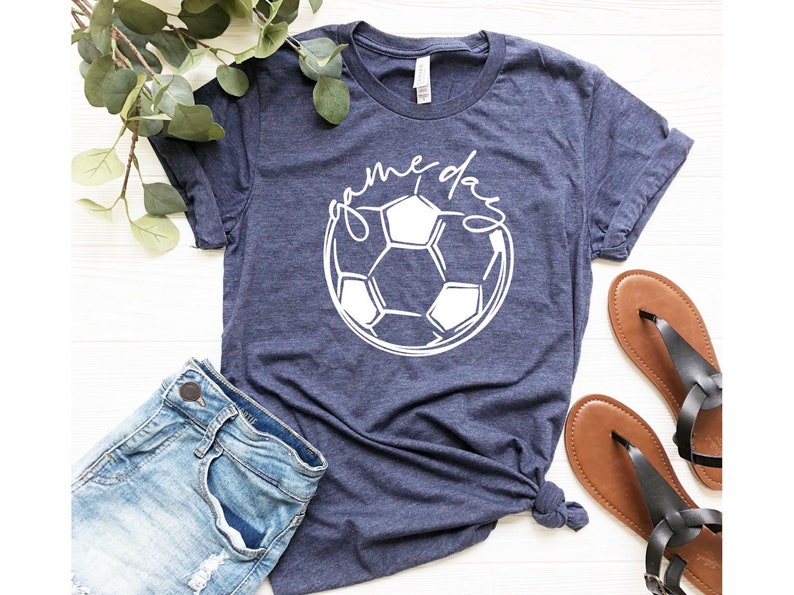 May include: A navy blue t-shirt with a white soccer ball graphic and the text "game day" written in a cursive font.