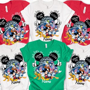 May include: A collection of short-sleeved t-shirts in red, white, and green. Each shirt features a colorful graphic of Disney characters, the text "Disney Trip 2026", and the name "Name".