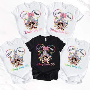 May include: Five white and one black t-shirts with a Disney theme. Each shirt features a colourful design with Mickey Mouse, a castle, and the text "2026 Name Disney Family Trip". The design is framed by a rainbow-coloured outline.