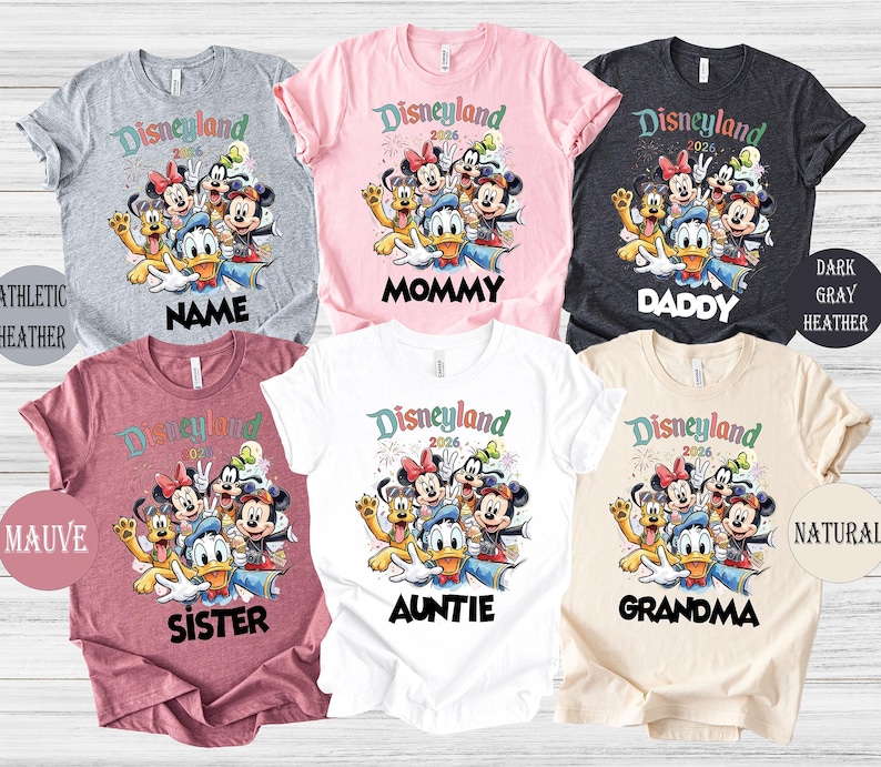 May include: Assorted-color Disneyland 2026 graphic t-shirts. The shirts feature a cartoon image of Mickey Mouse, Minnie Mouse, Donald Duck, and other Disney characters. Text on the shirts includes "Name", "Mommy", "Daddy", "Sister", "Auntie", and "Grandma".