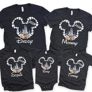 May include: A set of five dark grey t-shirts featuring a white Mickey Mouse silhouette and a castle graphic. The shirts are labelled with the text "Daddy", "Mommy", "Sophia", "Baby", and "Tommy". The year "2025" is also printed on each shirt.