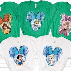 Puede incluir: Camisetas verdes y blancas con dise&ntilde;os de princesas de Disney. Cada camiseta muestra una princesa dentro de una silueta de oreja de Mickey Mouse con un lazo. Las princesas incluyen a Bella, Cenicienta, Anna, Blancanieves y Elsa.