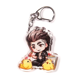 Puede incluir: Un llavero de acrílico transparente con un personaje de anime chibi de pelo negro, que lleva una camisa negra y sostiene palillos. El personaje está sentado con dos pollitos amarillos a cada lado. El llavero tiene un anillo de metal plateado.