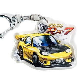 May include: A yellow Mazda RX-7 FD3S keyring with a silver key ring. The keyring features a cartoon illustration of the car with the text "FD3S RX-7" and a rotary engine logo.