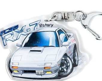 Op de afbeelding: Een witte Mazda RX-7 sleutelhanger met een blauwe en witte cartoon-illustratie van de auto. De sleutelhanger heeft een zilveren metalen ring en een transparante acryl achtergrond. De tekst "Rotary" is op de sleutelhanger gedrukt.