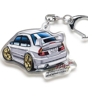Op de afbeelding: Een witte Mitsubishi Lancer Evolution VII RS sleutelhanger met een gouden velg en een zilveren sleutelring. De sleutelhanger heeft Japanse tekst die "Lancer Evolution VII RS" luidt.