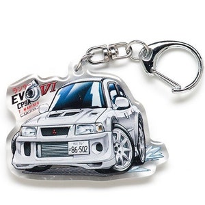Op de afbeelding: Witte Mitsubishi Lancer Evolution VI sleutelhanger met een cartoonillustratie van de auto. De sleutelhanger heeft een zilveren metalen ring en een transparante acryl achtergrond. De auto heeft een zwart kenteken met de tekst "*86-502" en de tekst "ランサー EVO CP9A T.マキネン EDITION" in het Japans.