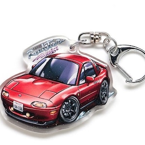 May include: Red Mazda MX-5 keychain with a silver key ring. The keychain features a cartoon illustration of a red MX-5 with the words "Edition Roadster NAGOYA" printed on the top.