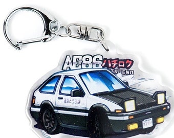 May include: White and black car keychain with the text "AE86 Initial D TRUEND" and Japanese text. The keychain is made of clear acrylic.