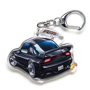 Op de afbeelding: Een zwarte Mazda RX-7 FD3S sleutelhanger met een zilveren sleutelring. De auto is afgebeeld in een cartoon-stijl met vlammen die uit de uitlaat komen. De sleutelhanger heeft de tekst "FD3S RX-7" en "54-383" erop gedrukt.