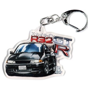 Op de afbeelding: Een zwarte Nissan Skyline R32 GT-R sleutelhanger met een zilveren sleutelring. De sleutelhanger heeft een witte achtergrond met rode en zilveren letters die "Skyline R32 GT-R" zeggen.