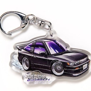 Op de afbeelding: Een zwarte en zilveren sleutelhanger met een cartoonillustratie van een zwarte Nissan 240SX met paarse accenten. De sleutelhanger heeft de tekst "SIL80 S13シルエイティ" in paars.