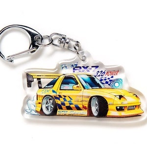 May include: A yellow and black car keyring with a silver key ring. The car is a cartoon illustration of a yellow sports car with black racing stripes and the text "RX-7 326 POWER" on the side.