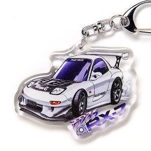 Op de afbeelding: Witte Mazda RX-7 sleutelhanger met een zwarte motorkap en paarse accenten. De sleutelhanger is gemaakt van helder acryl en heeft een cartoonachtige illustratie van de auto.