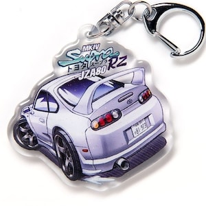 Può includere: Portachiavi Toyota Supra MKIV JZA80 RZ bianco con un anello portachiavi argentato. Il portachiavi presenta un'illustrazione a fumetti dell'auto con il testo "MKIV Supra トヨタスープラ JZA80 RZ" in alto.