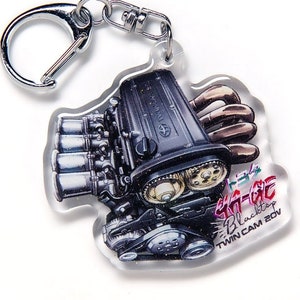 May include: A black and silver engine keychain with the text "4A-GE Blacktop TWIN CAM 20V" and Japanese characters. The keychain is made of clear acrylic and has a silver metal ring.