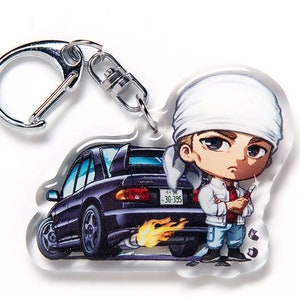 May include: A black and white anime-style keychain featuring a cartoon character wearing a white bandana and a white jacket, standing next to a black car with a Japanese license plate that reads "30-395".