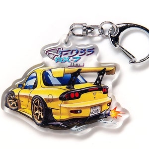 Op de afbeelding: Gele sportwagen sleutelhanger met een zilveren sluiting. De sleutelhanger heeft een gedetailleerde illustratie van een gele FD3S RX-7 auto met een achterspoiler, gouden velgen en de tekst "FD3S RX-7". De auto stoot vlammen uit de uitlaat.