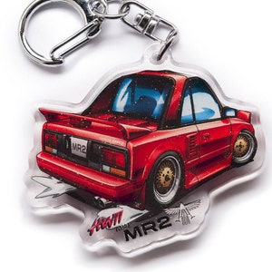 Op de afbeelding: Een rode Toyota MR2 sleutelhanger met een zilveren sleutelring. De sleutelhanger is gemaakt van helder acryl met een glinsterende afwerking. De auto is afgebeeld in een cartoon-stijl op een witte achtergrond.