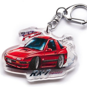 Op de afbeelding: Een rode RX-7 sportwagen sleutelhanger met een zilveren sleutelring. De sleutelhanger is gemaakt van helder acryl en heeft een cartoonillustratie van de auto met de tekst "RX-7 Turbo" en "FC3S" erop gedrukt.