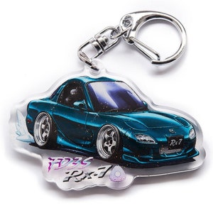 Op de afbeelding: Een turquoise blauwe Mazda RX-7 sleutelhanger met een zilveren sleutelring. De sleutelhanger heeft een gedetailleerde illustratie van de auto met een glinsterende afwerking. De tekst "FD3S RX-7" is op de sleutelhanger gedrukt.