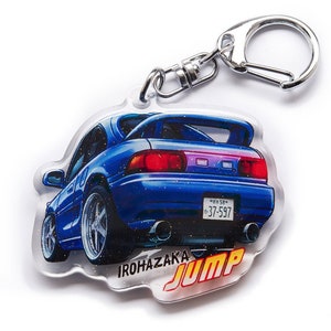 Op de afbeelding: Een blauwe en zilveren autosleutelring met een blauwe auto, een zilveren sleutelring en de tekst "IROHAZAKA JUMP" onderaan.