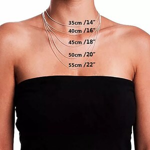 Puede incluir: Una persona con un top negro sin tirantes muestra una colecci&oacute;n de delicados collares plateados. Los collares var&iacute;an en longitud, con medidas de 35 cm (14"), 40 cm (16"), 45 cm (18"), 50 cm (20"), y 55 cm (22").