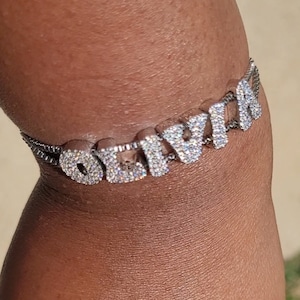 May include: A silver chain bracelet with the word "Olivia" spelled out in large, clear rhinestones.