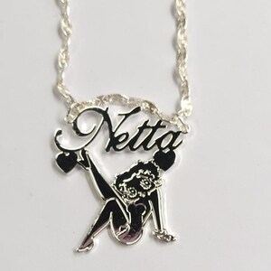 May include: Silver necklace with a silver pendant featuring a cartoon character and the name "Netta" in cursive.