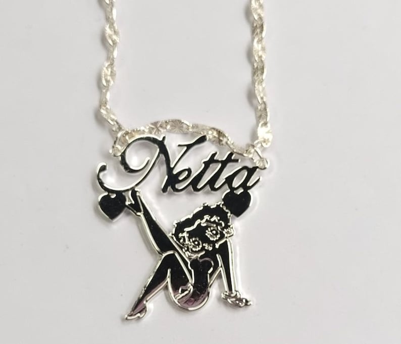 May include: Silver necklace with a silver pendant featuring a cartoon character and the name "Netta" in cursive.