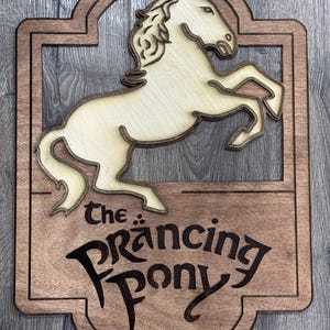 Op de afbeelding: Een houten bord met een gesneden afbeelding van een galopperend paard. Het bord heeft de tekst "The Prancing Pony".
