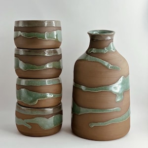 May include: A set of three ceramic mugs with a speckled, matte finish in cream, light grey, and dark grey. Each mug has a simple, minimalist design and a rounded handle.