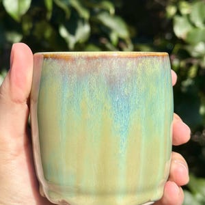 May include: A green and yellow ceramic mug with a brown rim. The mug has a textured, wavy glaze.