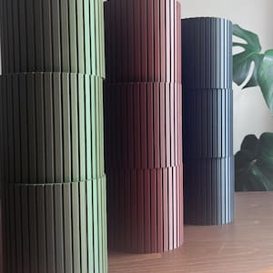 May include: Three cylindrical containers with vertical ribbed textures, arranged in a row. The first is olive green, the second is deep maroon, and the third is dark charcoal gray. Each container is composed of three stacked segments.