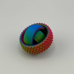 May include: A colorful, 3D-printed sphere with a textured, spiky outer ring in shades of red, yellow, and green. The inner ring is a smooth gradient of blue and green. The sphere is a unique, eye-catching decorative item.